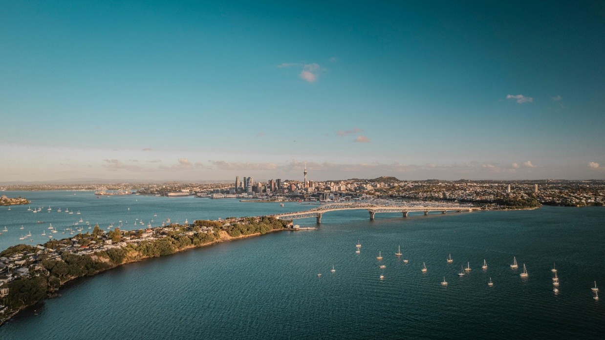 Aeria view of Auckland Harbor Bridge on sunn day. Dozens of boats dot the blue water.