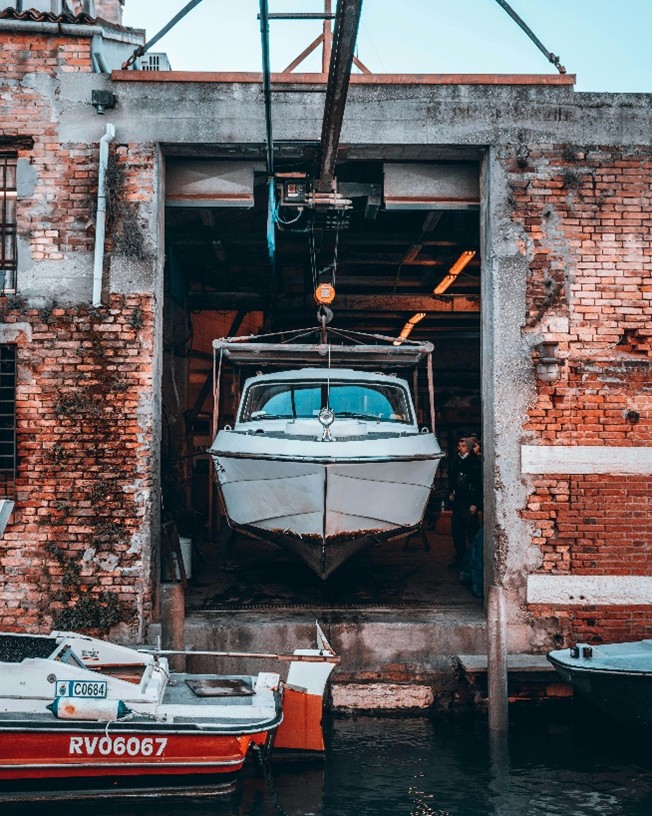 boat in canal in venice is on a lift at a service center (brick exterior building) located on the waters of the canal