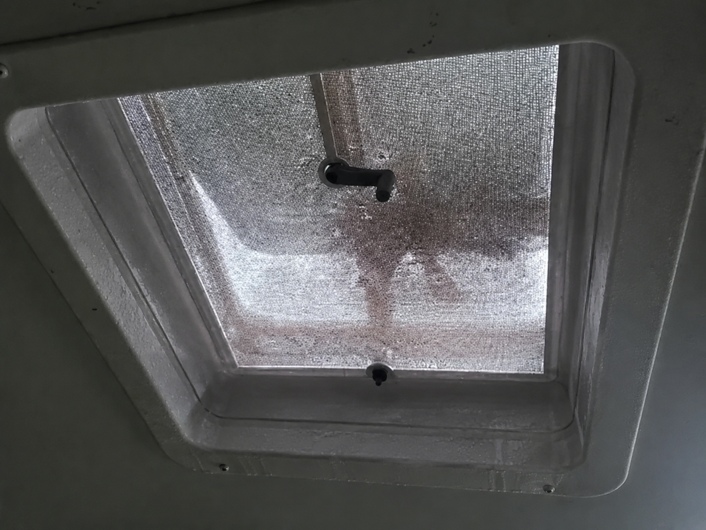 Condensation beads on a metal-framed boat or RV roof hatch, with water dripping down the frame.